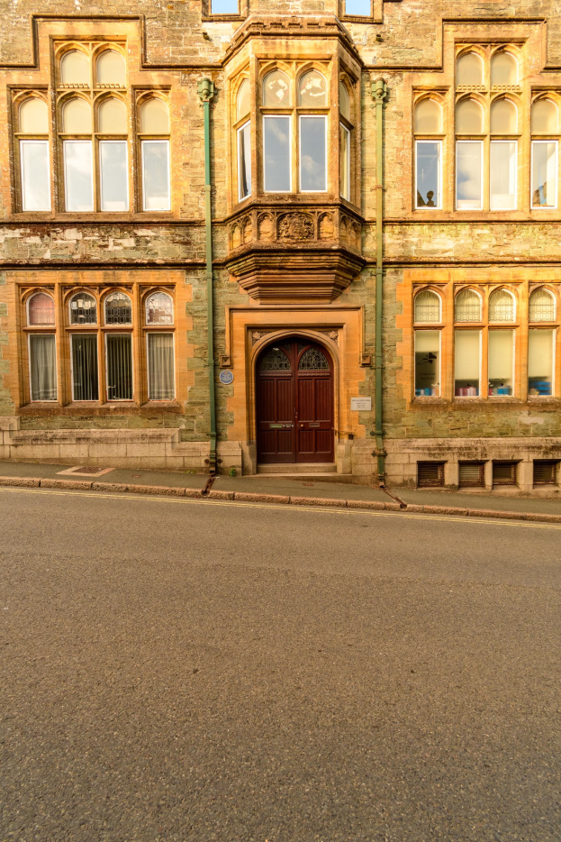 Altes Gebäude mit vielen Fenstern und einer hölzernen Tür an der Seite einer Straße, mit Rohren an seinen Wänden.