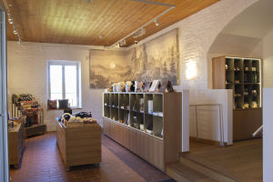 Ein Raum voller verschiedener Möbelstücke, einschließlich eines Tisches mit Gegenständen, Regalen mit Gegenständen, einem Foto Rahmen an der Wand, einem Fenster, Deckenleuchten und einer Treppe, Teil eines neuen Ladens in Heidelberg, Deutschland.