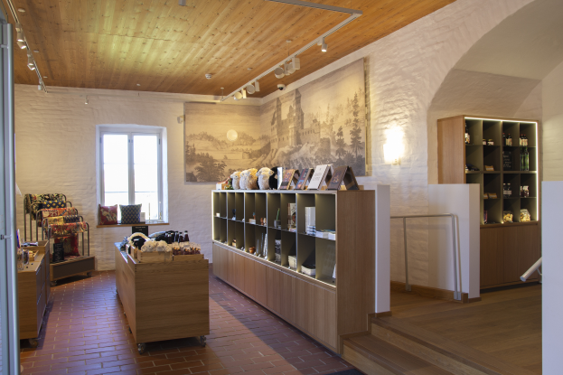 Ein Raum voller verschiedener Möbelstücke, einschließlich eines Tisches mit Gegenständen, Regalen mit Gegenständen, einem Foto Rahmen an der Wand, einem Fenster, Deckenleuchten und einer Treppe, Teil eines neuen Ladens in Heidelberg, Deutschland.