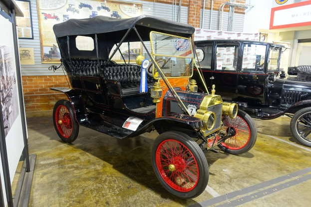 Ein Oldtimer in einem Museum ausgestellt mit Informationsschildern, Deckenleuchten und sichtbarem Rad.