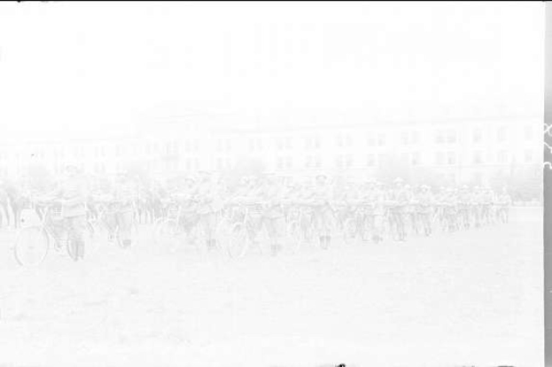 Schwarzes und weißes Foto von Radrennfahrern, die an einem Gebäude vorbei fahren.