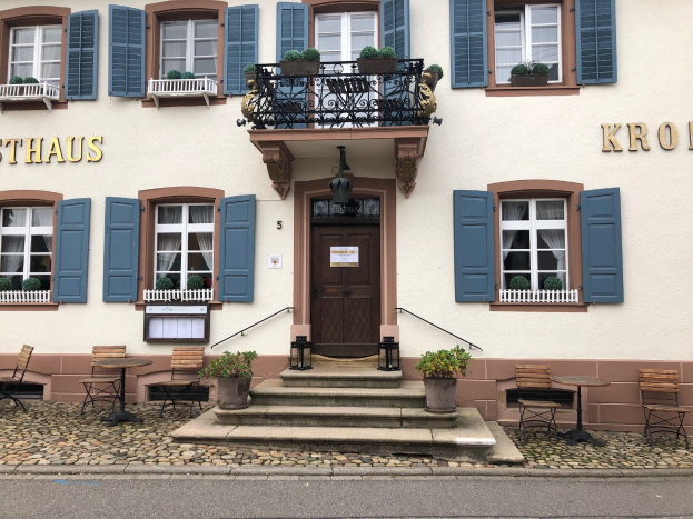 Ein zweistöckiges Gebäude in Sthaus, Deutschland mit blauen Fensterläden, Fenstern, Türen, Geländern, Topfpflanzen, Gartenmöbeln, Treppen und einer nahen Straße.